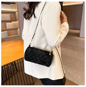 Detail of black velvet quilted cylinder bag with a gold chain strap on a white blazer