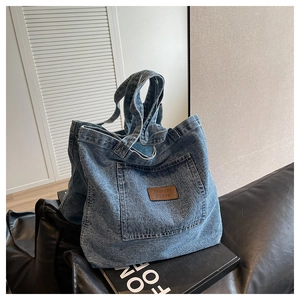 Détail du sac cabas en denim bleu avec étiquette en cuir sur un canapé en cuir noir