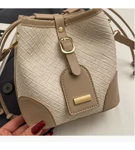 Close-up of beige woven bucket bag with brown leather trim and golden metal clasp buckle