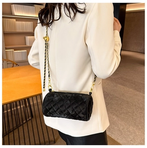 Detail of black quilted velvet cylindrical bag with golden chain and ball slider