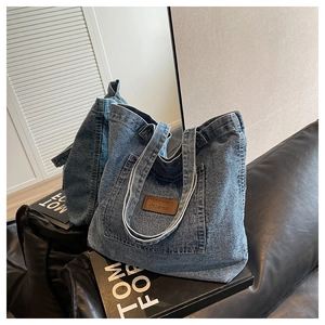 Détail d'un sac cabas en jean bleu avec écusson en cuir et poche avant sur canapé