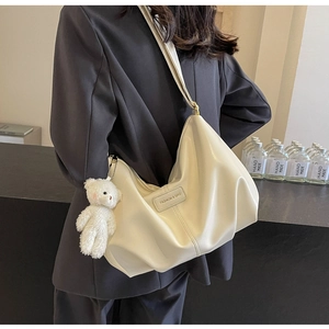 Detail of cream white pleated tote bag with plush bear charm and fashion label