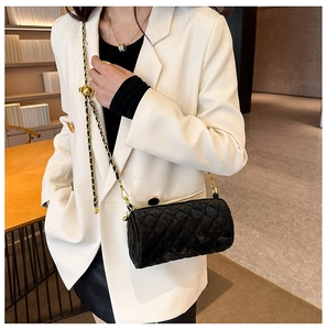 Quilted black cylinder crossbody bag with gold chain strap shown on white blazer