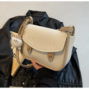Detail of cream saddle bag with leather texture, dual buttons and plush monster charm