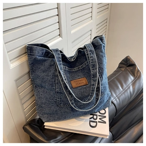 Gros plan d'un sac cabas en jean bleu avec écusson en cuir marron et détails de tissu texturé