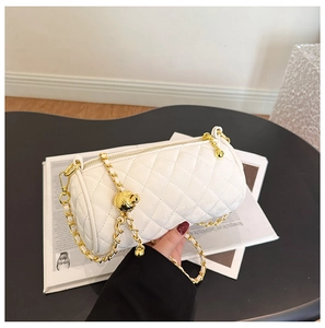 Close-up of white quilted cylinder bag featuring a gold chain strap and metal ball charm