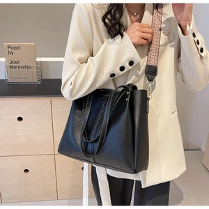 Detail view of black faux leather tote bag with contrast stitching and woven strap