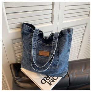 Détail du grand sac cabas en jean bleu délavé avec écusson en cuir et poche externe