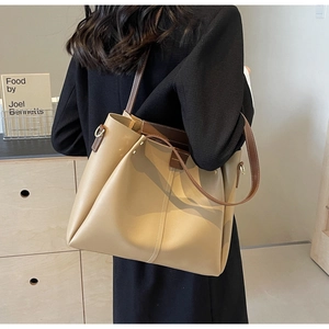 Detail of a large khaki tote bag with brown leather straps shown on a model's shoulder