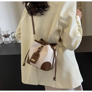 Detail of woven straw bucket bag with brown leather trim and drawstring on model