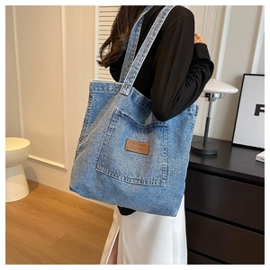 Detailed view of casual denim tote bag with front pocket and brown leather logo tag