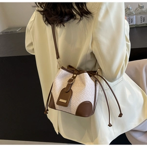 Beige woven bucket bag with leather drawstring and gold buckle shown on shoulder