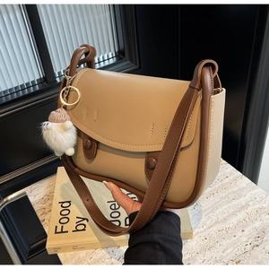 Detail of two-tone leather saddle bag with plush pompom charm and elegant flap closure
