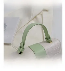 Detail of white crocodile-embossed handbag with green leather handle and gold hardware
