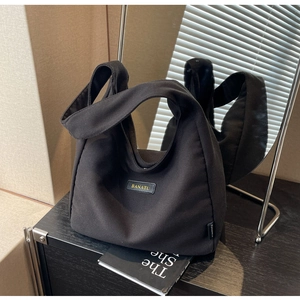 Close-up of minimalist black canvas tote bag with leather logo patch and side label