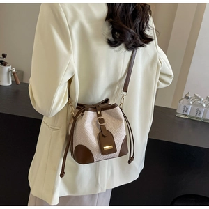 Detailed shot of a woven bucket bag with brown leather trim and golden metal buckle