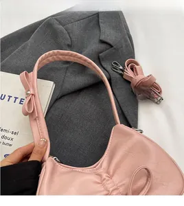 Detail of pink pleated underarm bag featuring decorative bows and versatile straps