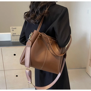 Detailed close-up of brown tote bag showing the wide geometric fabric strap and gold hardware