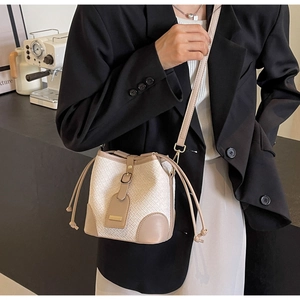 Detail view of cream woven bucket bag with brown leather trim on model in black blazer