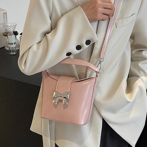 Sac seau rose avec fermoir nœud argenté porté par un mannequin en tailleur beige