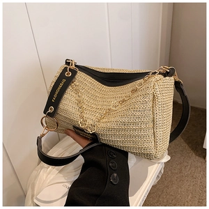 Close-up of woven straw Boston bag featuring black leather straps and gold metal chain