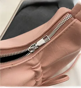 Detailed close-up of smooth silver metal zipper on pleated light pink leather shoulder bag
