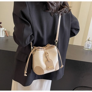 Detail of beige woven and brown leather bucket bag styled with a black blazer