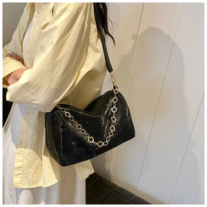Detail of glossy black Boston bag featuring gold floral chain and textured leather