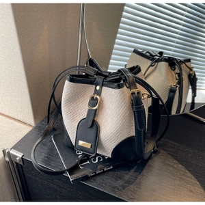 Detailed macro view of woven beige bucket bag with black leather trim and gold metallic buckle