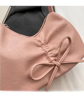 Detail of pink faux leather bag featuring a decorative bow and pleated texture