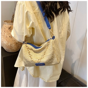 Detailed close-up of woven straw Boston bag with blue leather trim and golden flower chain