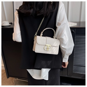Detail of cream crocodile pattern handbag with gold chain strap worn by a model