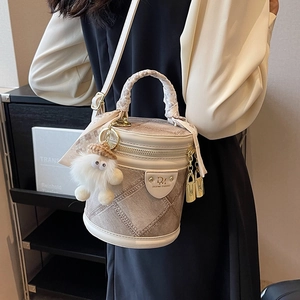 Quilted beige bucket bag with plush charm and woven handle shown in a lifestyle setting