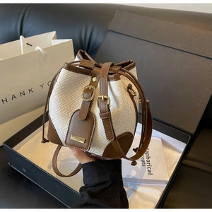 Close-up of cream woven bucket bag with brown leather trim and golden metal clasp