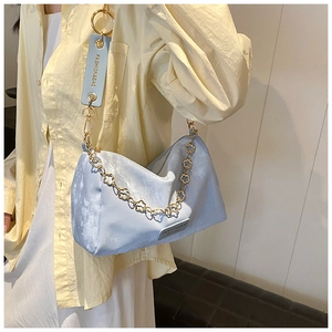 Detail of light blue Boston bag featuring golden flower chain and wide leather strap