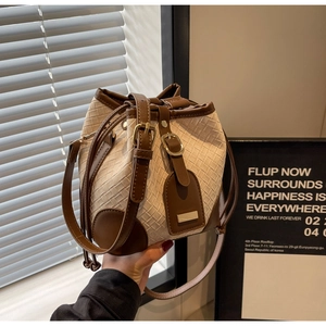 Detailed close-up of woven bucket bag with brown leather trim and metallic buckle accents