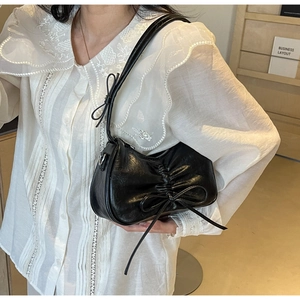 Close-up of black ruched shoulder bag with bow ribbon detail on model in lace shirt
