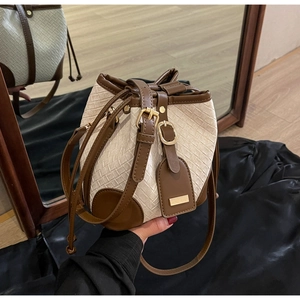 Detail of woven bucket bag featuring brown leather trim and golden metal drawstring buckle