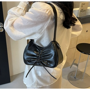 Detail of black pleated crescent shoulder bag with bow, shown on model in modern interior