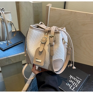 Detail of cream woven bucket bag showing faux leather trim and drawstring closure