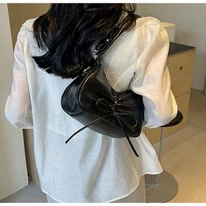 Detail view of black underarm bag with bow tie and ruched side on white linen top