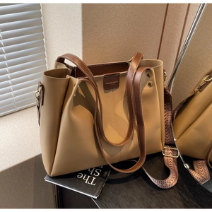 Detail of khaki tote bag with brown handles and wide printed shoulder strap on desk
