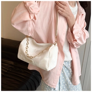 Detail of white plush Boston bag with gold flower chain and fashion label on soft fabric