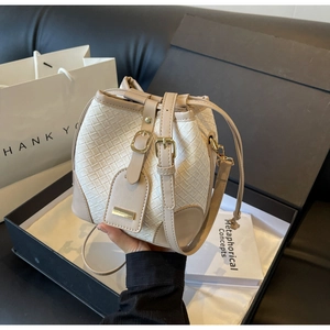 Close-up of beige woven texture bucket bag with leather trim and gold metal plate