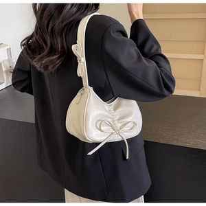 Close-up of cream pleated shoulder bag with bow details on a black blazer outfit