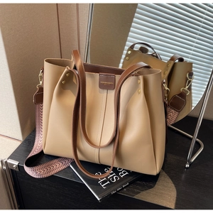 Detail of beige tote bag showing woven strap, brown trim, and premium metallic hooks