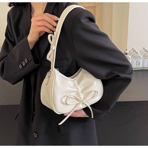 Close-up of creamy white ruched shoulder bag with bow details on black blazer