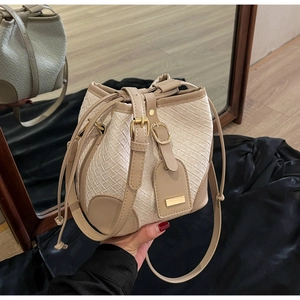 Detail of woven straw bucket bag with drawstring closure and khaki leather accents