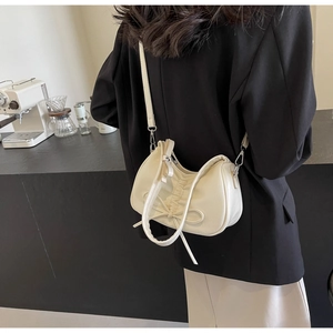 Chic cream ruched shoulder bag with bow detail shown on model in a modern cafe setting