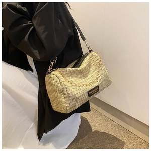 Detail of straw woven Boston bag featuring black leather straps and gold chain decor